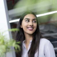 Portrait of young Latin-American businesswoman sitting at computer in office, looking away and smiling