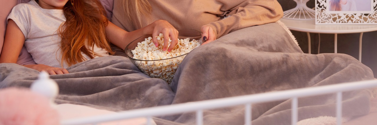 Mother and daughter watching film in bed, eating popcorn