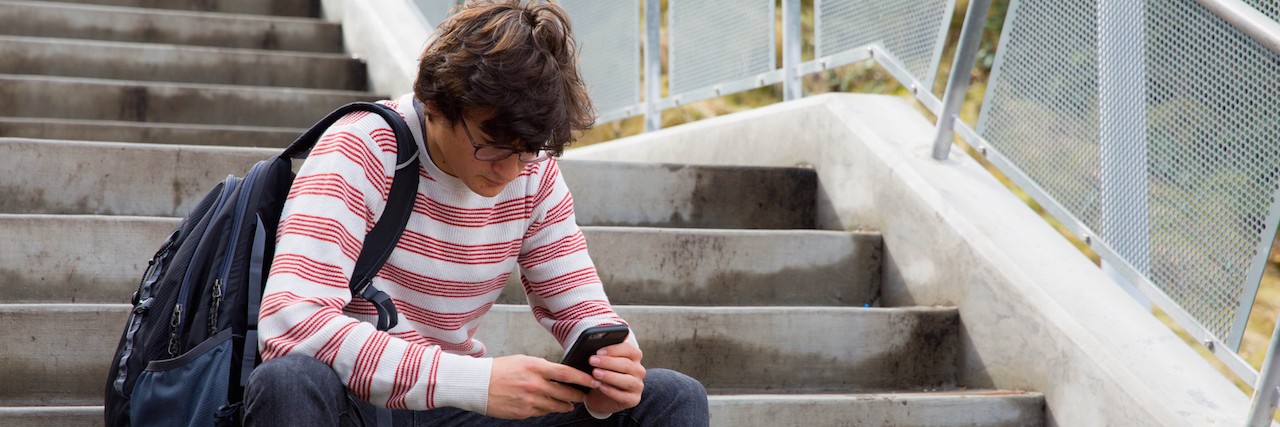 Letter to a Kid With Depression Who Compares Himself to Everyone teen sitting on steps, looking at this phone