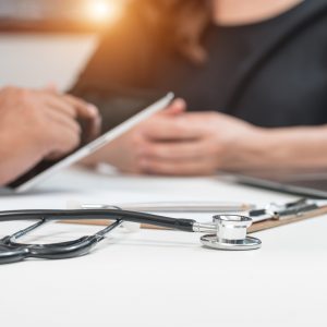 Close-up of doctor holding tablet, sitting at desk across from patient
