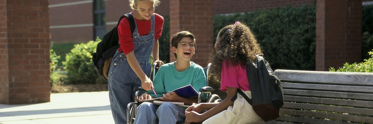 Boy in a wheelchair talking to two girls outdoors