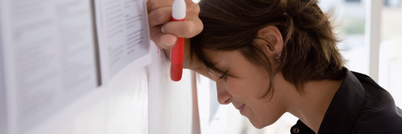 Chronic Illness: What It's Like to Have Brain Fog woman leaning her head against a dry erase board and looking frustrated