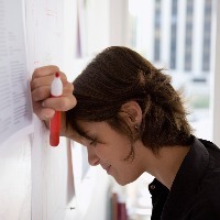 woman leaning her head against a dry erase board and looking frustrated