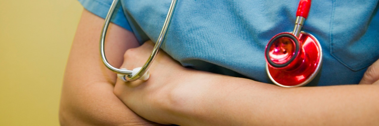 12 Things a Doctor With Chronic Illness Wants People to Know a doctor with crossed arms in scrubs with a stethoscope around their neck