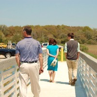 Three people, two men one woman in a bright blue dress, walking on a footbridge. They are facing away from the camera.