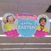 Easter display ad hanging from Walgreen's ceiling, has two children in eggs. A young girl with Down syndrome and a young boy.