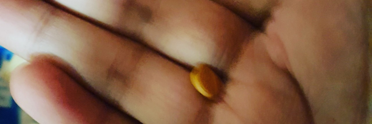 picture of a hand with a yellow pill int he middle