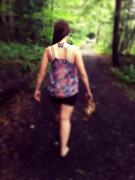 woman with a butterfly tattoo walking barefoot on a path through the woods