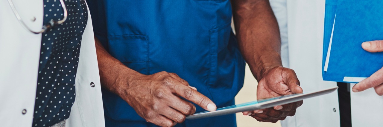 A Letter to Doctors From a Patient With Crohn's Disease Group of doctors standing consulting patient records on a tablet computer, close up view