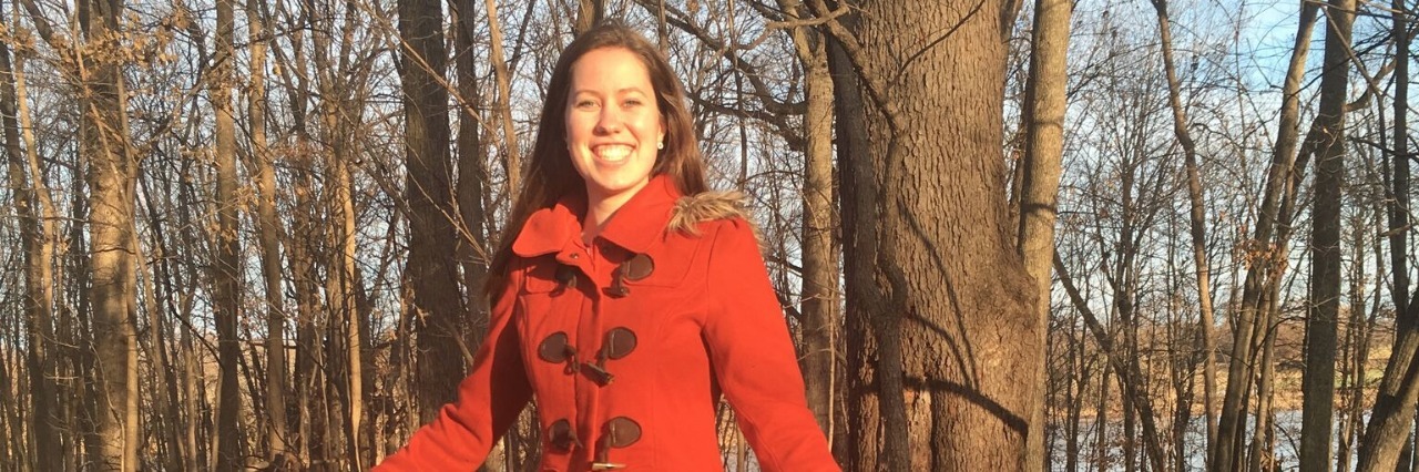 Changing Your Attitude Toward Life With Chronic Pain woman in red coat standing on a tree stump in the woods