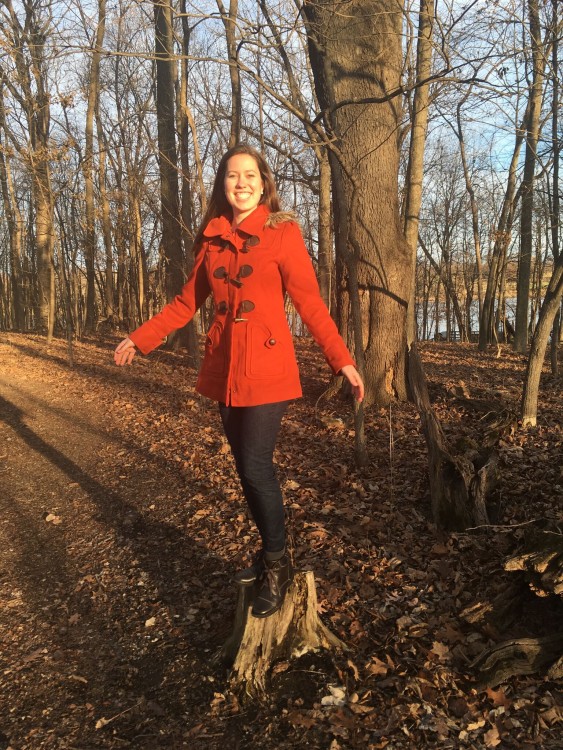 woman in red coat standing on a tree stump in the woods