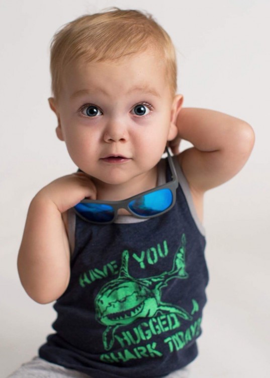 Little boy wearing a navy blue shirt and sunglasses around his neck