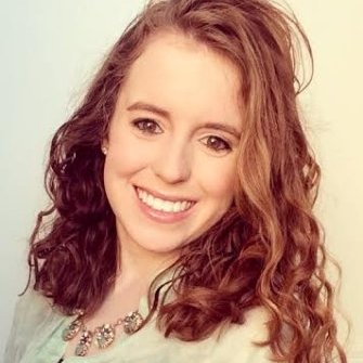 A young woman with red hair looks at the camera with a smile.