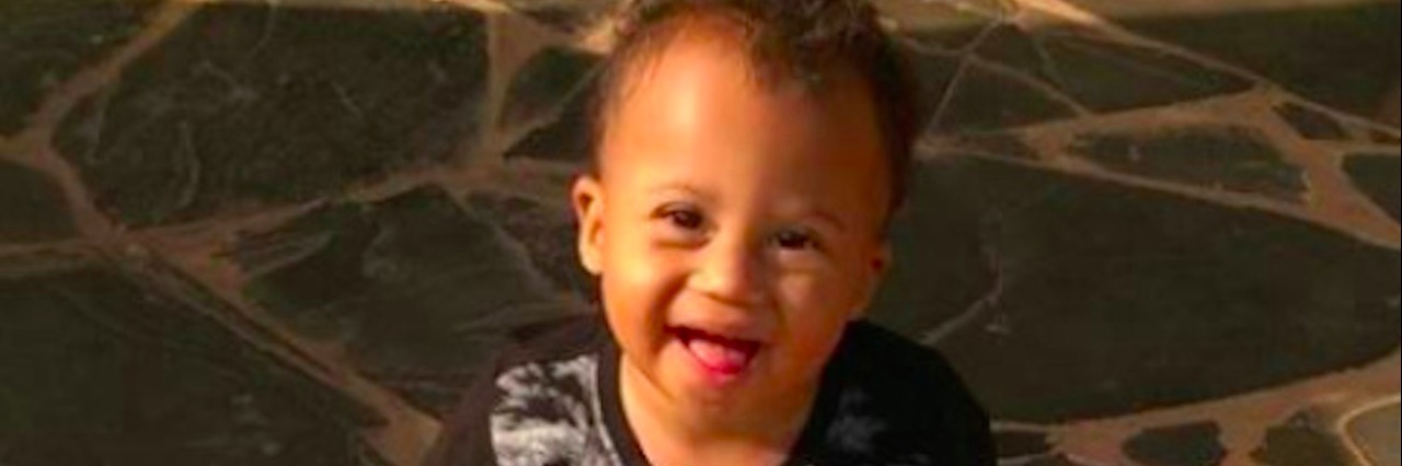 Responding to Assumptions as a Mom of a Child With Down Syndrome Boy sitting on a step outside, smiling at camera