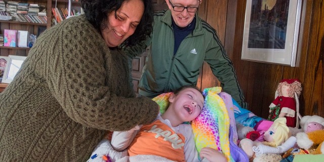 Mother and father with daughter in living room. Mother is holding daughter's hand, and all three are smiling. Photo courtesy of photographer Ed Hille