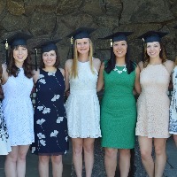 seven young women in dresses smile and wear graduation hats