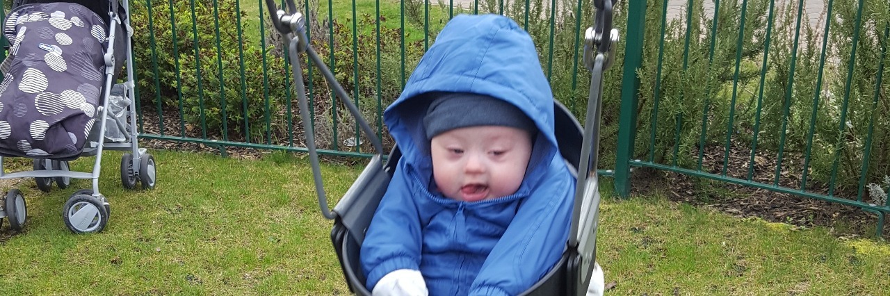 Baby with Down syndrome wearing a blue jacket and swinging outdoors