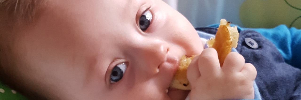 What Does It Mean When the Doctor Asks If My Son Is Thriving? Baby with Down syndrome sitting in a bouncy chair wearing a blue jumper and gumming a piece of bread