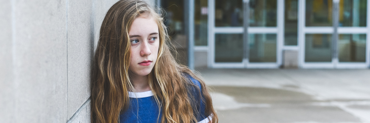 How My High School Coach Showed Stigma About My Anxiety and Depression photo of high school female student leaning against wall looking upset