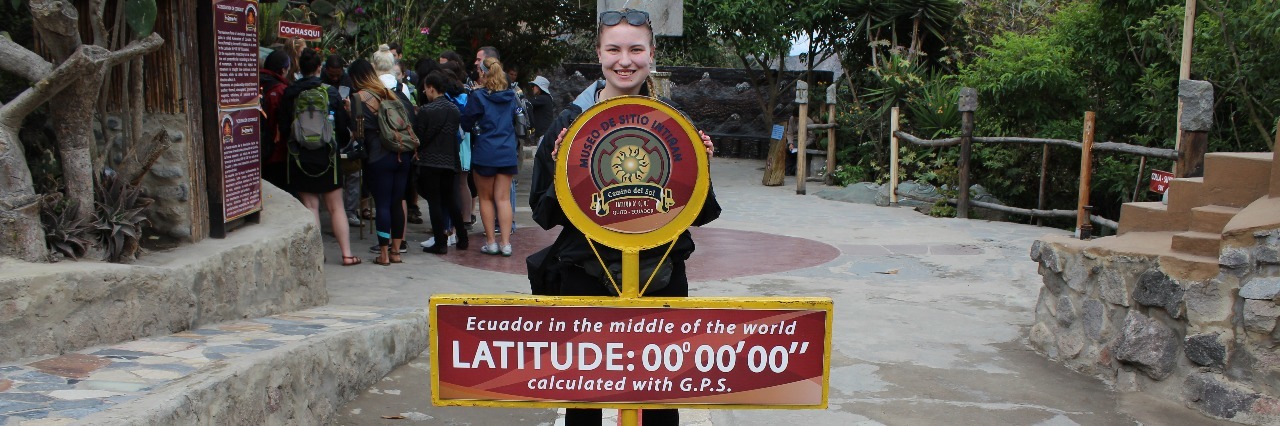 Tips for Studying Abroad With Chronic Pain or Illness woman standing next to marker for zero degrees latitude in ecuador