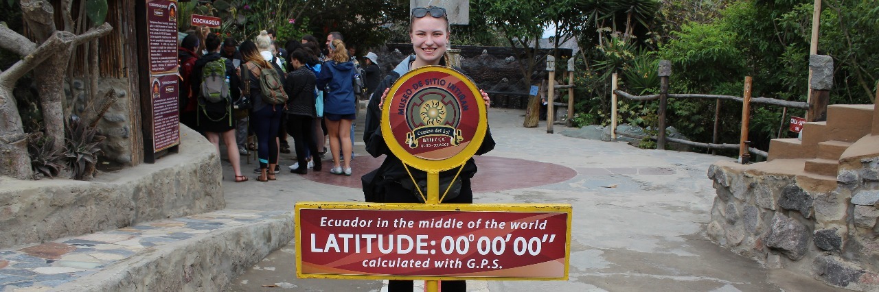 woman standing next to marker for zero degrees latitude in ecuador