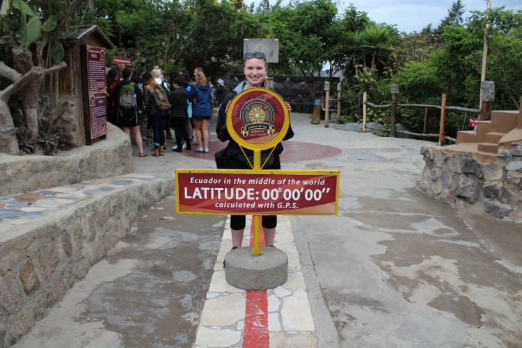 woman standing next to marker for zero degrees latitude in ecuador