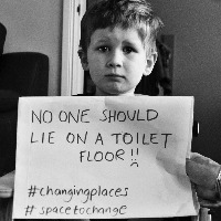 Boy holding sign that reads "No one should lie on a toilet floor."