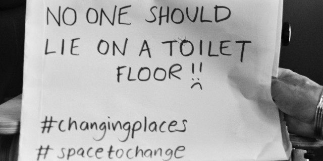 Why I'm Campaigning for Changing Places Toilets During Disability Awareness Month Boy holding sign that reads "No one should lie on a toilet floor."