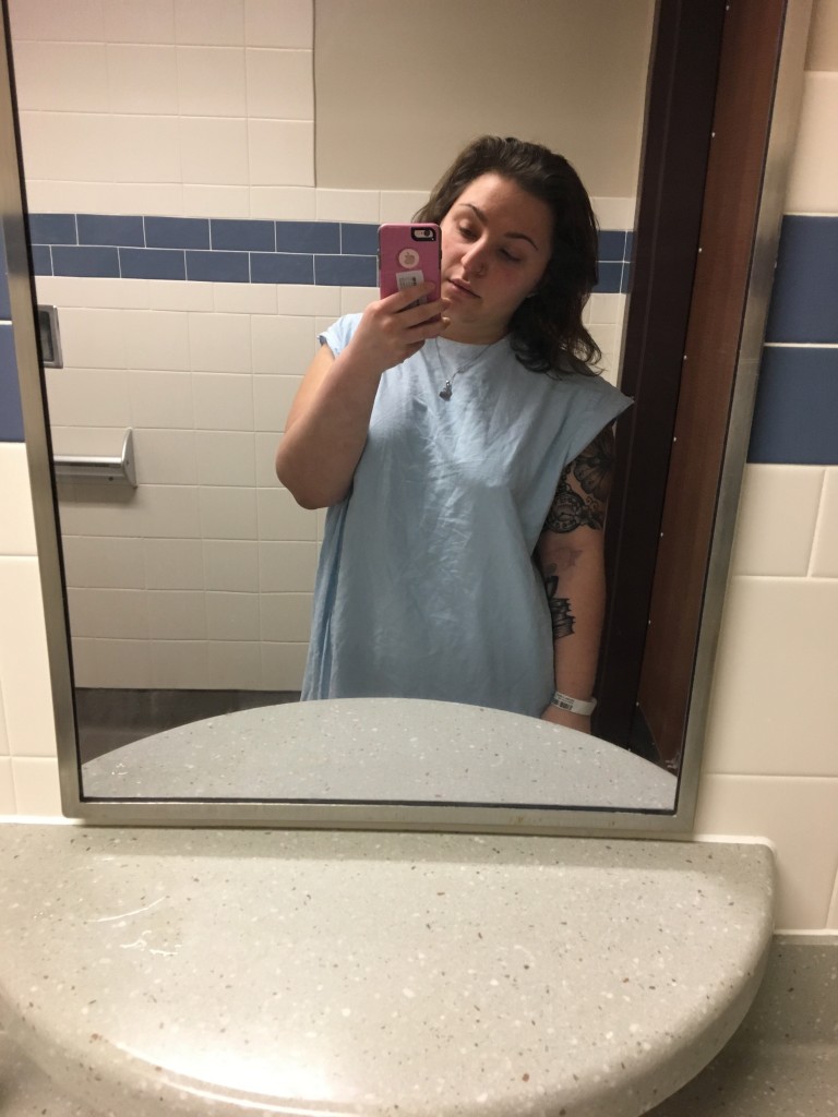 author looking into mirror wearing blue hospital gown in psych ward