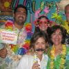 A group of 5 people in a photo booth wearing silly hats, over-sized glasses, in a Hawaiian themed background