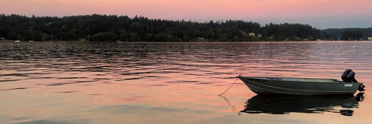 A rowboat sits in a middle of a lake with a beautiful sunset behind