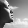 Black and white photo of profile of woman's face with eyes closed, cloudy sky background