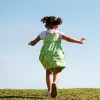 Child running up grassy hill with blue sky in the background