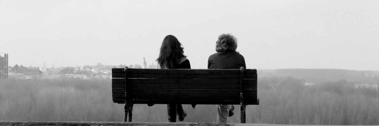 Two people sitting on bench in black and white