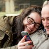 Father and teenage daughter with head in his shoulder sharing something funny in a mobile phone