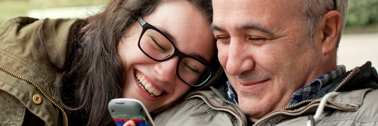 A Letter to My Dad, Who Supported Me in My Journey With Chronic Pain Father and teenage daughter with head in his shoulder sharing something funny in a mobile phone