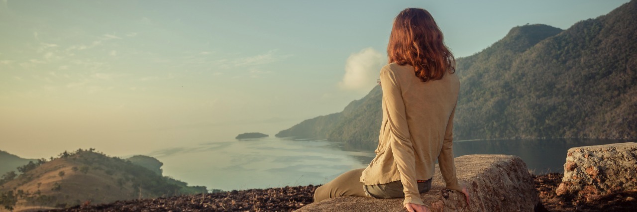 woman sitting on a rock overlooking a lake and mountains at sunrise
