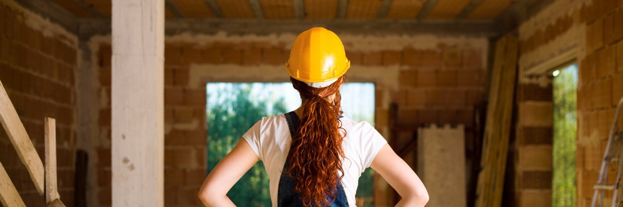 female bricklayer with her hands on her hips looks at house under construction