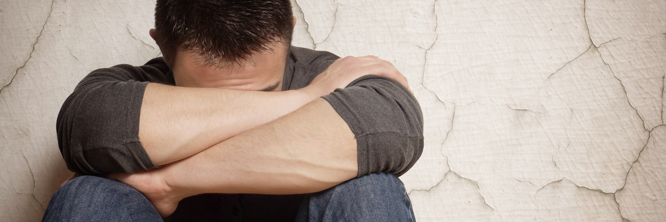 What It's Like to Live With Dissociative Identity Disorder man hiding face in arms leaning against cracked wall