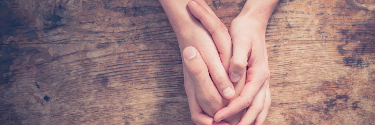 Trauma Survivors Need to Support Each Other on the Internet Close up on a man and a woman holding hands at a wooden table