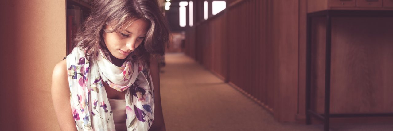 Why Universities Need to Better Support Students With Mental Illness Female student reading a book in the library aisle