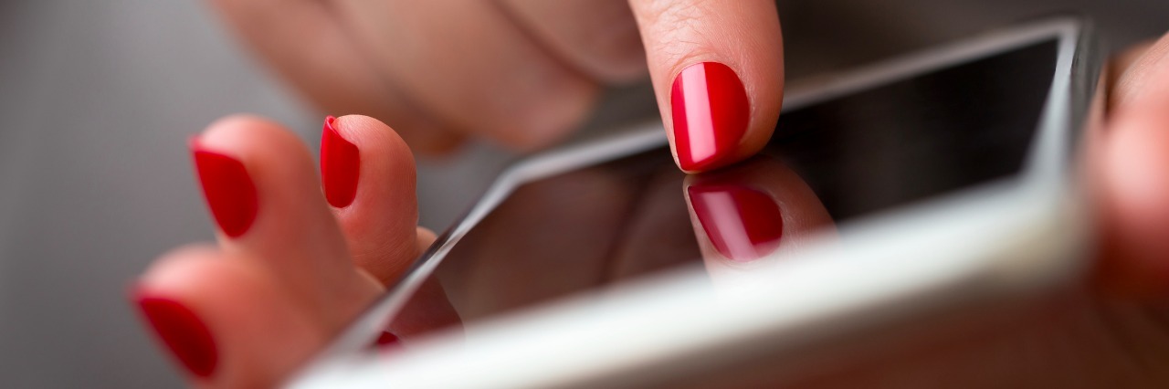 Why I Post on Social Media So Much as a Woman With an Illness Closeup of a woman hand using smart phone, focus on finger with red nail polish typing on the screen , shallow depth of field.