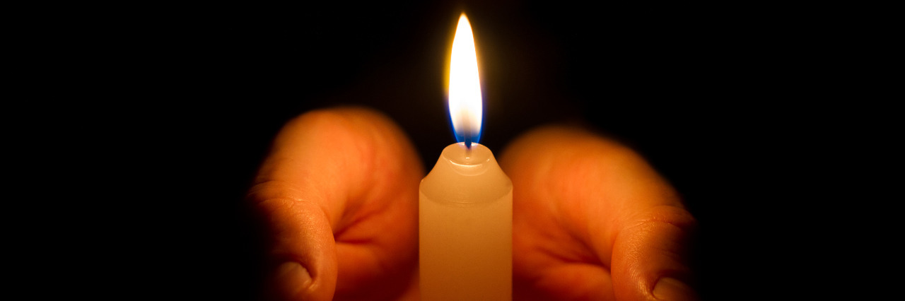 Finding Unity in These Dark Times for People With Disabilities Hands holding a lit candle in the darkness.