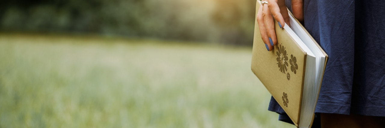 The Value About Being Open About Disability Woman holding a journal looking toward the sunset.