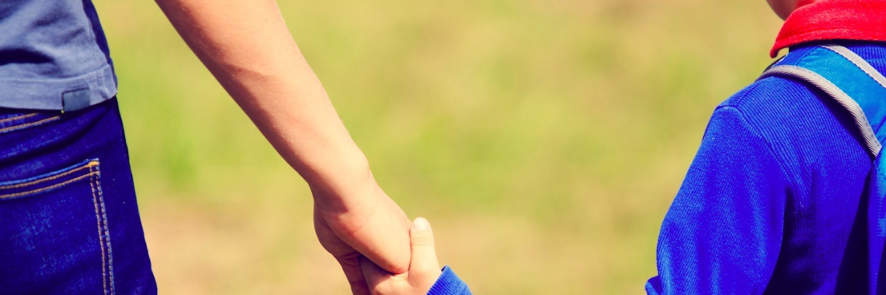 The Courage I See Every Day in My Son on the Autism Spectrum Mother holding hand of son, who is wearing a backpack, as they walk together outdoors
