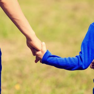 Mother holding hand of son, who is wearing a backpack, as they walk together outdoors