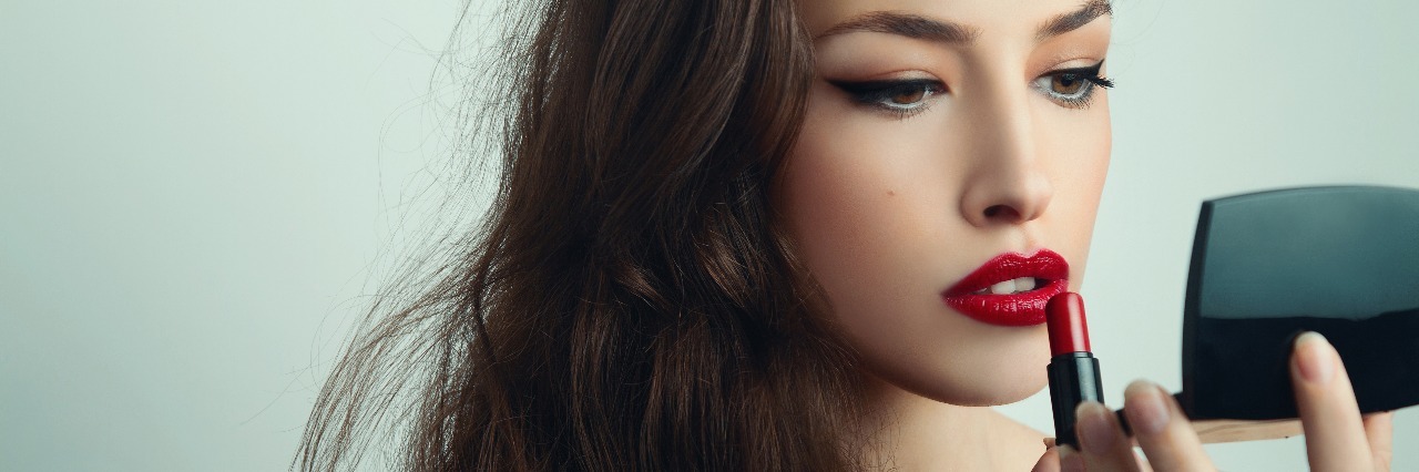 Why I Use Makeup as a Form of Self-Care Woman with long hair applying red flipstick
