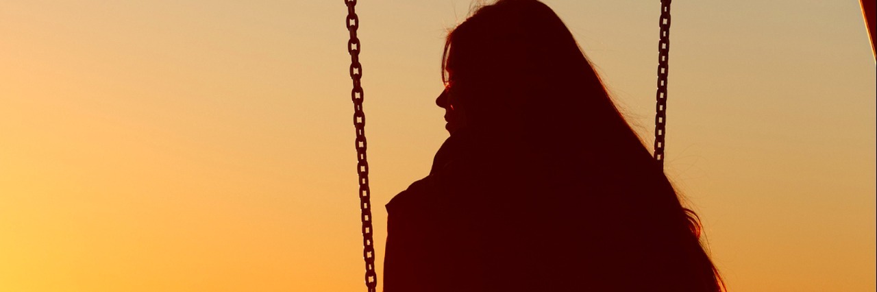 Silhouette of woman on swing, facing sunset sky