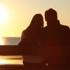 silhouette of woman and man sitting on a bench in front of the ocean watching the sunset