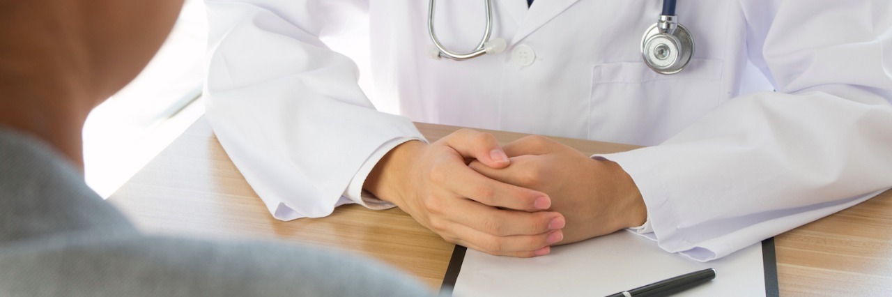 The Importance of Being Believed by Doctors Doctor with hands on desk, sitting in front of patient